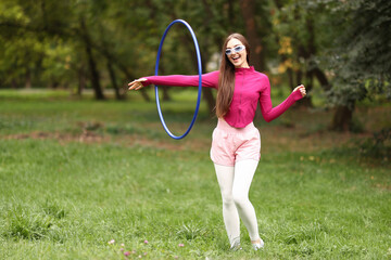 Athletic young woman exercising with hula hoop in park © New Africa