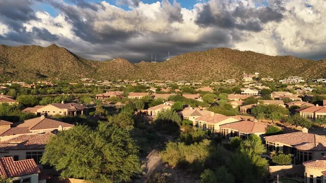 4K drone view over the Las Sendas community in Mesa, Arizona, surrounded by rugged desert mountains beneath dramatic clouds and warm sunlight.