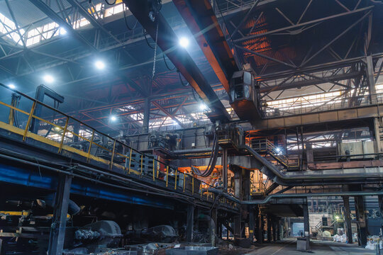 Crane spans steel factory hall above industrial machinery in pipe mill infrastructure for manufacturing.