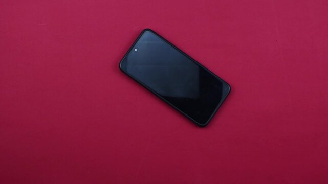 La mano de un hombre coloca un tel&eacute;fono m&oacute;vil sobre una mesa roja
