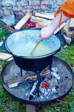 A hand is stiring in a kettle with onions above a campfire to prepare onion soup.