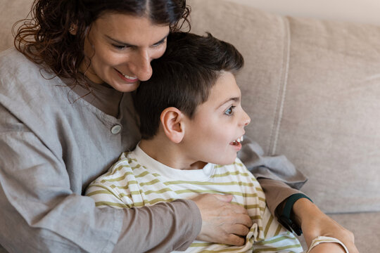 Mother embracing son with cerebral palsy on sofa