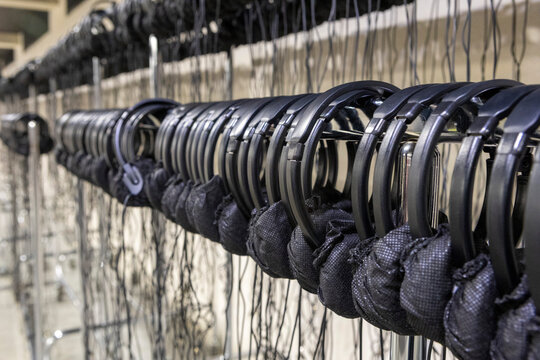 Row of black fishing net floats threaded on metal rings hanging from dockside railing along pier edge in harbor setting under bright coastal daylight with crisp shadows