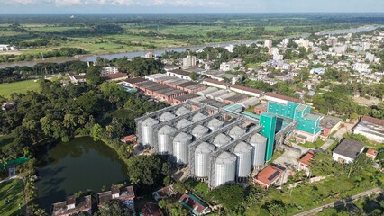 Aerial view of a large industrial grain silo facility located near a river and residential area in a rural landscape © ridwanhassan