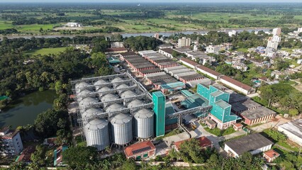 Aerial view of a large industrial grain silo complex and processing facility located near a river in a rural landscape with surrounding greenery © ridwanhassan
