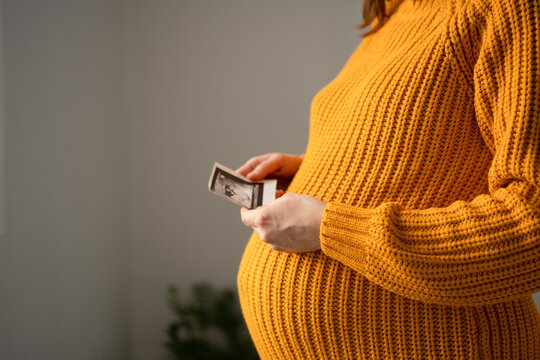 A pregnant woman in profile examines an ultrasound photo of her baby scan. The expectant mother viewing a sonogram presents a tender, joyful moment of first glimpse and loving anticipation.