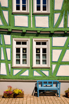 Charming green and white half-timbered facade with traditional windows, blue bench and flowers in the historic old town of Idstein, Hesse, Germany.