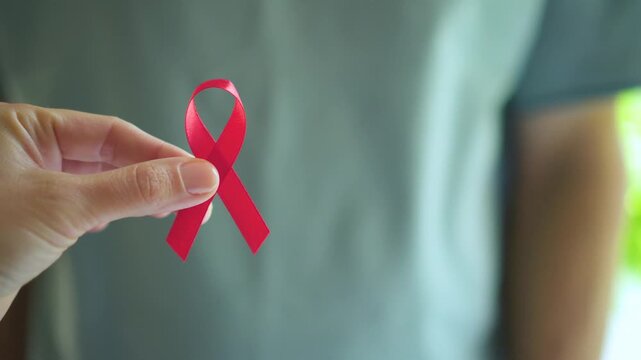 Mans hand carefully holding red satin ribbon symbolizing HIV AIDS awareness support for affected people and December hope.