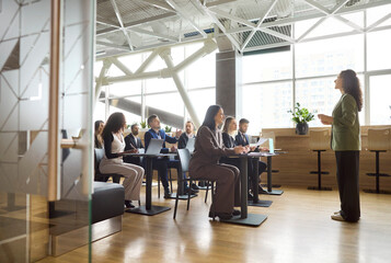 Naklejka na ściany i meble Speaker leads training seminar for office team. Engaged audience in a meeting listens to a coach giving a presentation in a bright modern workspace. Clear concept of team learning workshop.