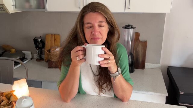 Middle aged woman pensively drinking coffee or tea and enjoying a moment of peaceful calm