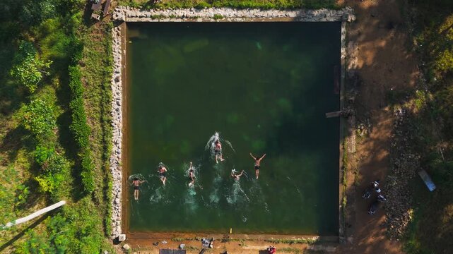 Aerial view of Embung Mbalong with people swimming in the square reservoir surrounded by trees in Kecamatan Banyubiru, Jawa Tengah, Indonesia.