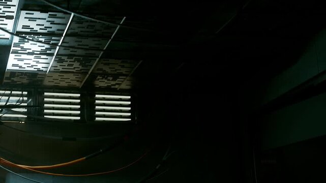 A dimly lit interior shows a ceiling with patterned panels and a wall with vents. Wires hang from the ceiling, creating a scene of industrial design and structure.