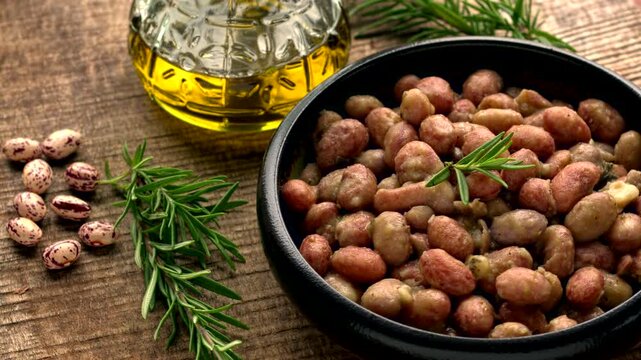 Traditional Tuscan recipe featuring freshly shelled soft Borlotti beans, rosemary, and olive oil in a bowl, with the main ingredients displayed on a dark brown, weathered, unplaned pine sawmill board.
