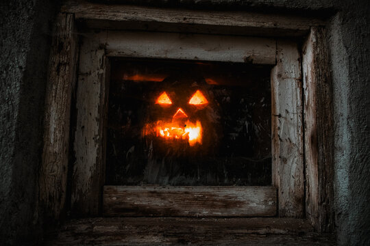 scary Halloween pumpkin glowing in window at night