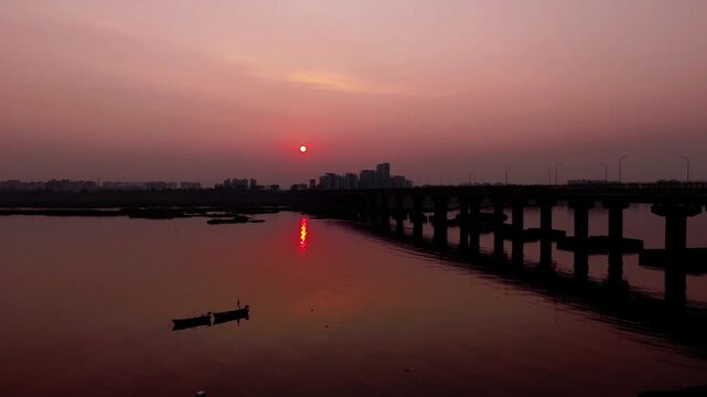 Aerial view of the Tapi River at sunset with a bridge, small boats, and the city skyline in the background in Surat, Gujarat, India.