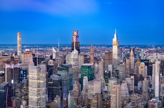 At dusk, an elevated panorama of Midtown Manhattan in New York City, United States, reveals dense rows of buildings, glowing windows and prominent towers stretching toward the distant horizon.