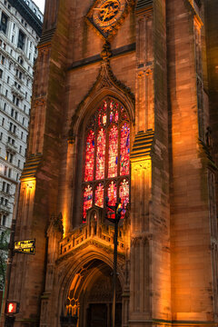 View showing details of colorful stained glass windows and Neo-Gothic architecture at Trinity Church in downtown Manhattan New York illuminated by warm light at night.