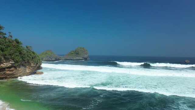 Emerald Green Capped Rock Islets Rising Triumphantly Above Energetic Ocean Waves and Shimmering Coastal Waters at Goa Cina Beach