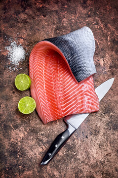 Fresh salmon red fish steak on rustic grunge table with knife and lime. Ready for sushi cooking japanese food. Top view.