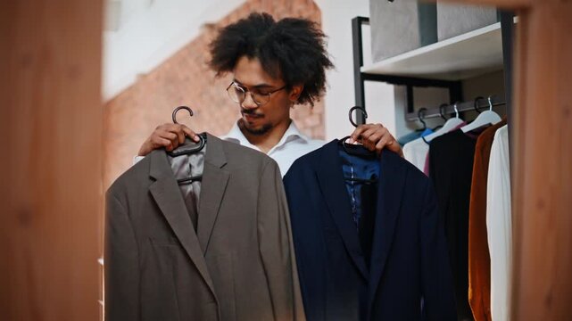 Shop assistant holding two blazers hangers. Boutique menswear clothing store.