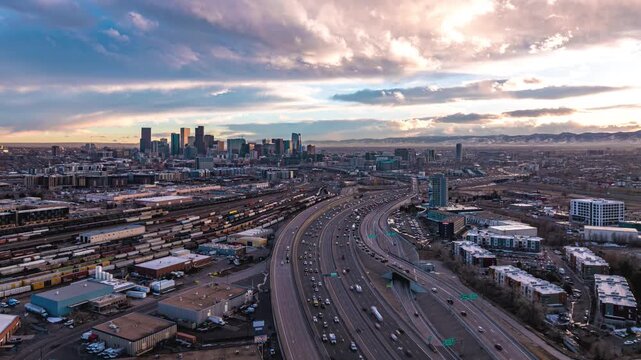 Denver, United States - 10 September 2025: Aerial view of the Denver skyline, busy highway traffic, and extensive railway yards under a dramatic sunset sky.