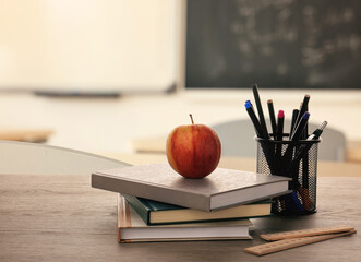 Books, apple and stationery on desk in classroom. Space for text © New Africa