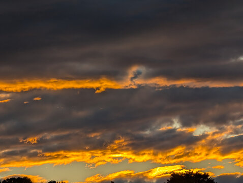 Golden sunset light breaks through layers of dark clouds in a dramatic evening sky