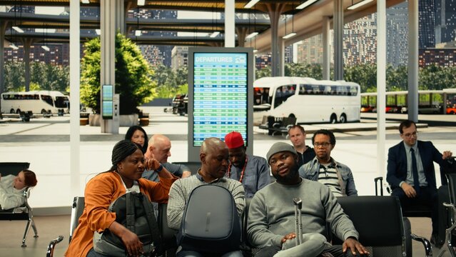 Tired passengers yawn and wait at a crowded bus terminal after delayed departures, while diverse travelers sit with backpacks near the departure board in an intercity coach hall during delays.