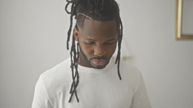 Young man face with dreadlocks and nose stud looking at camera in a studio wearing a white t shirt, subtle expression; thoughtful introspection.