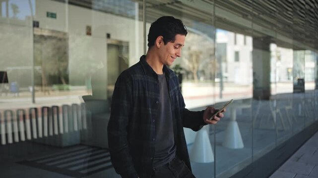 Young hispanic man using mobile phone reading good positive news, standing at office workplace
