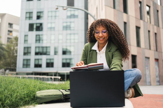 Modern business woman working on laptop sitting outdoors office building