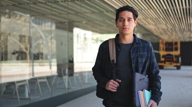 Portrait of young hispanic student carrying laptop books backpack standing inside university faculty building