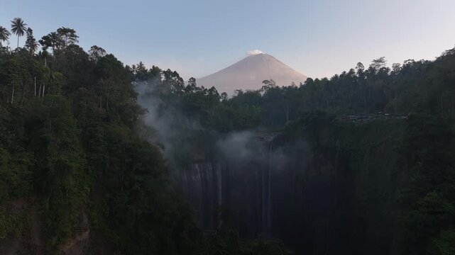 Kecamatan Pronojiwo, Indonesia - 01 September 2026: Aerial view of Tumpak Sewu Waterfall with Mount Semeru in the background, surrounded by lush tropical forest and mist.
