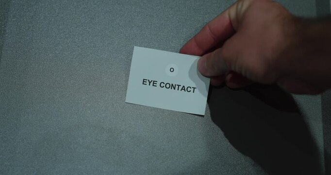 A hand holding an eye contact paper card against a gray background, representing attention, nonverbal communication and interpersonal connection