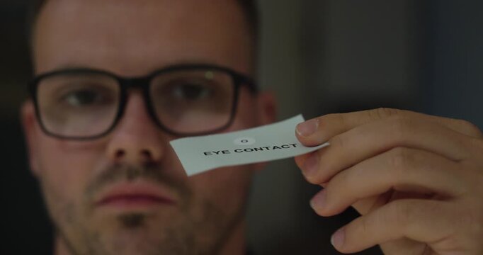 Man turns a card around to reveal the words &ldquo;Eye Contact,&rdquo; representing communication, body language, social interaction, confidence and interpersonal skills.
