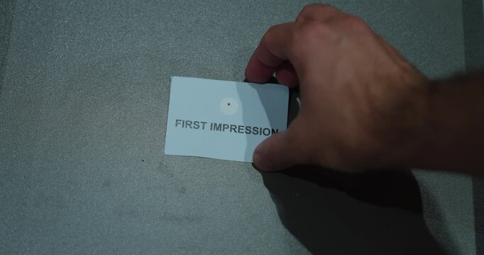 A hand holding a first impression paper card against a gray background, representing perception, introductions and social interaction