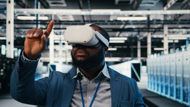 Server farm employee puts on a VR headset for network management while using virtual reality simulation to oversee data center infrastructure rigs.