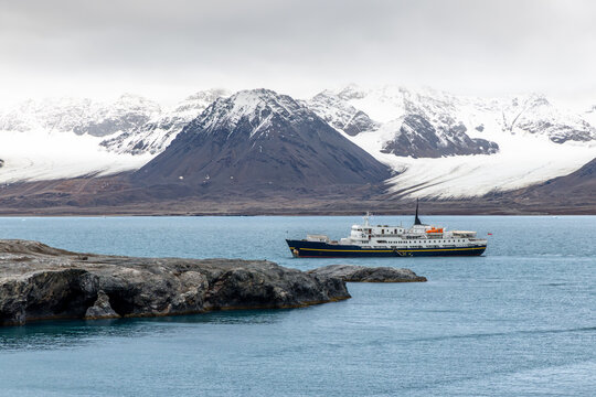 Passenger expedition ship sailing through a remote Arctic fjord beneath broad glaciers and dramatic snow-covered mountain ridges, Spitsbergen, Svalbard, Norway
