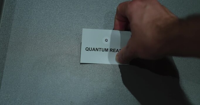 A hand holding a quantum realm paper card against a gray background, representing physics, scientific exploration and abstract concepts