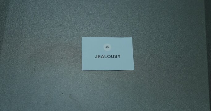 A drawer opens to reveal a card labeled Jealousy, which is then picked up by hand. Concept for jealousy, envy, human emotions, relationships and emotional awareness.