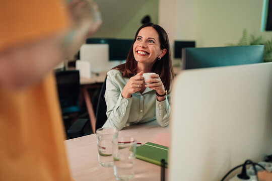 Happy business woman smiling during a meeting in modern office, enjoying coffee and conversation with colleagues
