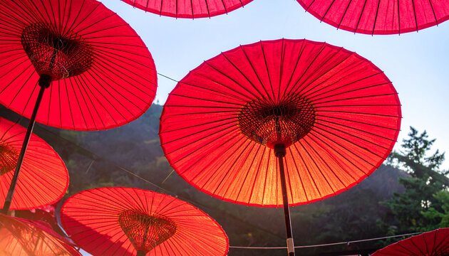 青空を背景に頭上で鮮やかに広がるたくさんの真っ赤な和傘のローアングル写真　光を透かして骨組みのシルエットが浮かび上がる幻想的で華やかな装飾の風景　日本の伝統行事の告知チラシや旅行サイトのバナー、和風デザインのWebサイトの背景、お祝い事のポスターや年賀状の素材