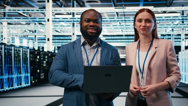 Engineering team works together with a laptop on server maintenance tasks in a high tech data center, configuring machine settings, checking equipment and supporting server infrastructure operations.