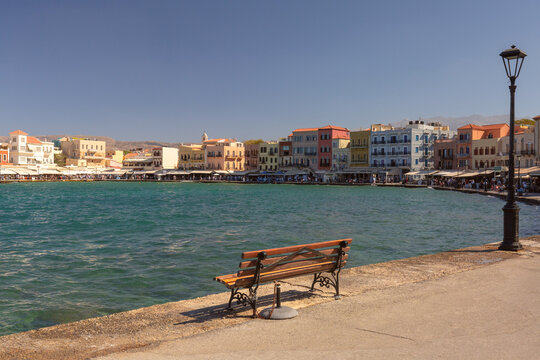 View across the Venetian Harbor toward colorful historic waterfront buildings and restaurants in Chania, Crete, Greece.