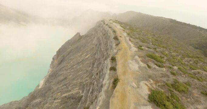 FPV aerial view of the rocky volcanic terrain and sparse vegetation along the Ijen Volcano ridge in East Java, Indonesia.