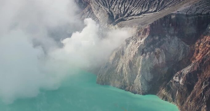 FPV aerial view of the turquoise crater lake and rocky cliffs of Ijen Volcano in East Java, Indonesia.