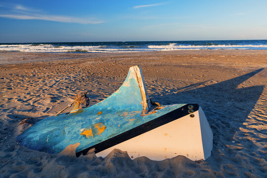 Peeling blue paint covers an overturned boat hull partially buried in beach sand.
