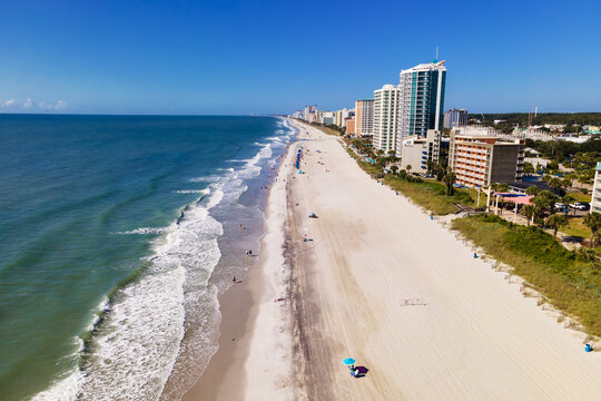 Open sand stretches beside waterfront buildings in a wide Myrtle Beach aerial panorama.