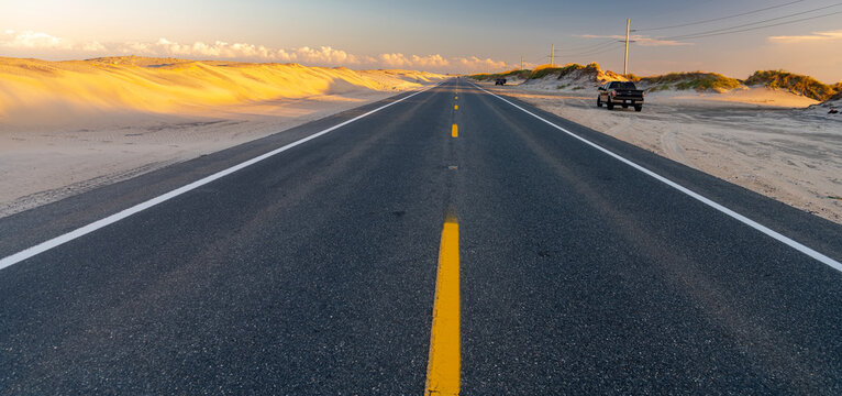 A yellow centerline dominates a low viewpoint along a North Carolina coastal highway.