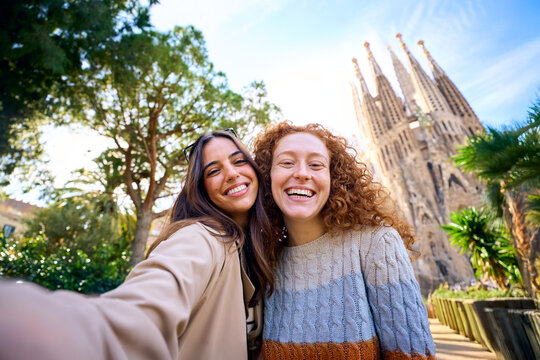 Young funny caucasian women friends taking selfie in front of Sagrada Familia in Barcelona. Beautiful girl on street of European city enjoying vacation happy and smiling. Funny tourism people